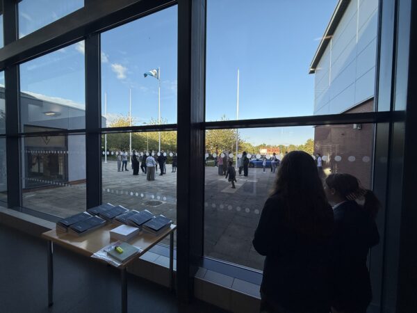 two students looking out of window onto queue of parents and students